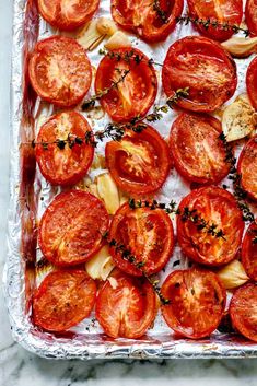 sliced tomatoes on a baking sheet ready to go into the oven with herbs sprinkled on top