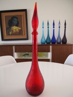 a red vase sitting on top of a white table in front of colorful glass bottles