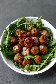 a white bowl filled with meatballs and greens on top of a black tablecloth