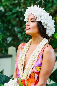 a woman with flowers in her hair is wearing a lei and holding a flower bouquet