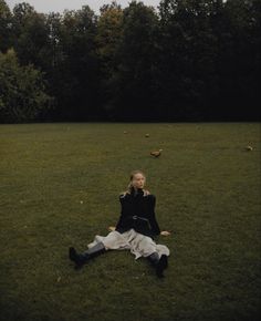 a woman sitting on the grass in front of trees