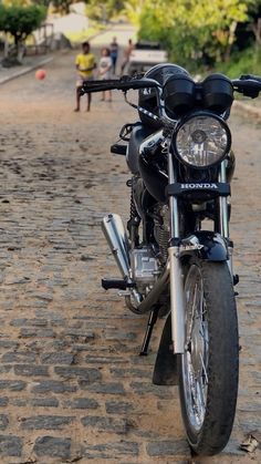 a black motorcycle parked on the side of a road with people walking in the background