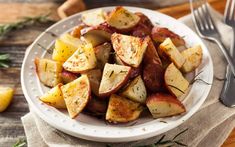 a white plate topped with potatoes on top of a table next to a knife and fork