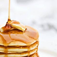 a stack of pancakes with syrup being poured on top and maple syrup pouring over them