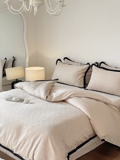 a bed with white sheets and black trim around the edges, in front of a large mirror