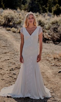 a woman in a wedding dress standing on a dirt road with trees in the background