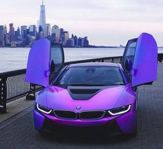 a purple car with its doors open next to the water in front of a city skyline