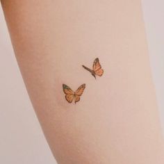 two small butterflies on the back of a woman's leg, one is orange