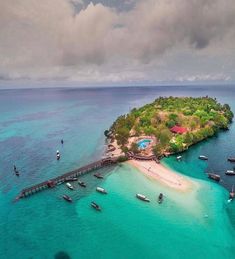 an island in the middle of water with boats floating on it's sides and a pier extending out into the ocean