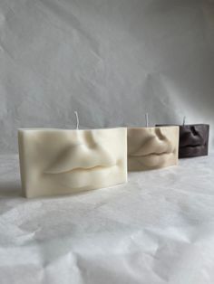 three square candles sitting next to each other on top of a white sheeted surface