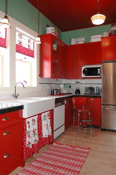 a kitchen with red cabinets and white counter tops is pictured in this image, there are two rugs on the floor next to the sink