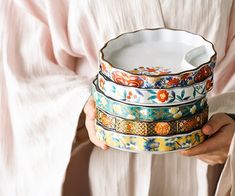 a woman holding a stack of colorful dishes in her hands