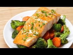 a white plate topped with salmon and broccoli on top of a wooden table