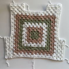 a crocheted square is sitting on the floor next to a white tablecloth