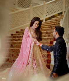 a man standing next to a woman in a pink and gold dress on top of stairs