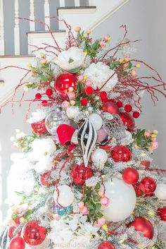 a decorated christmas tree with red and white ornaments on the top, in front of a staircase