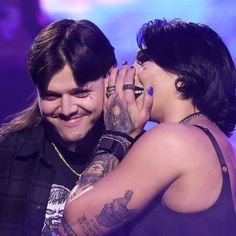 two people with tattoos on their arms and one is kissing the other's face