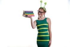 a woman in a green dress is holding some books and wearing a beetle costume on her head