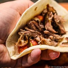 a hand holding a tortilla filled with meat and vegetables