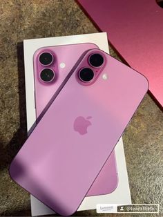 two pink iphones sitting next to each other on top of a table in front of a box