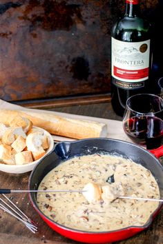 there is a bowl of soup and bread on the table next to two bottles of wine