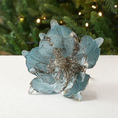 a blue flower sitting on top of a white table next to a green christmas tree