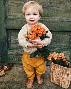 a little boy standing next to two baskets filled with orange roses and holding it in his hands