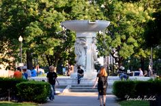 a woman walking down a sidewalk next to a white statue in the middle of a park