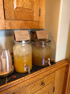 two jars filled with liquid sitting on top of a wooden cabinet next to a tea kettle