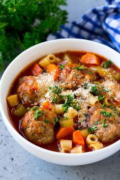 a white bowl filled with meatballs and pasta soup next to parmesan cheese