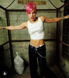 a woman with pink hair and piercings standing in a jail cell holding her arms out