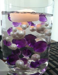 a glass vase filled with purple and white pearls next to a lit candle on top of a table