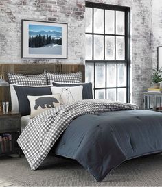 a bed with black and white comforters in front of a brick wall next to a window