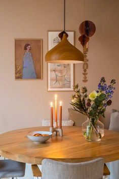 a dining room table with candles and pictures on the wall above it, along with two vases filled with flowers