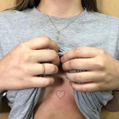 a woman with a heart tattoo on her chest holding onto the back of her shirt