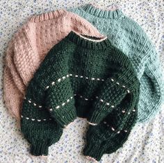 three knitted sweaters laying on top of a bed