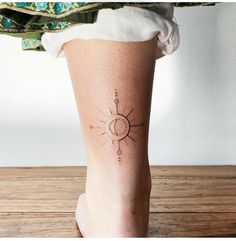 a woman's leg with a small sun tattoo on her left calf and an arrow in the middle