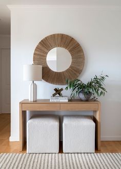 a living room with white furniture and a round mirror on the wall above two stools