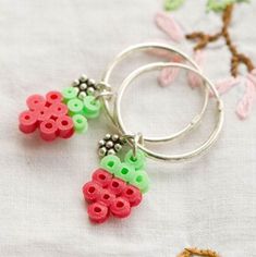 two pairs of earrings made out of plastic beads on a white tablecloth with flowers in the background