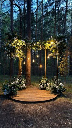 a wooden platform with flowers and lights on it in the middle of a wooded area