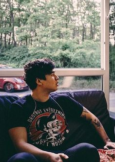 a man sitting on top of a couch in front of a window next to a red car