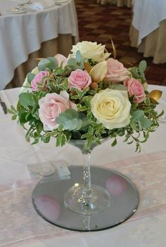 a glass vase filled with pink and white flowers on top of a table covered in tables cloths