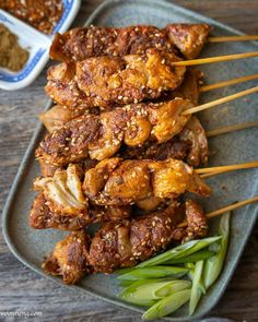 chicken skewers on a plate with dipping sauce and green onions in the background