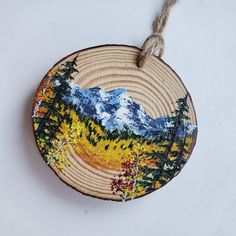 a round wooden ornament with mountains and trees painted on it