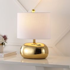 a gold lamp on a white table next to a vase with flowers and a book