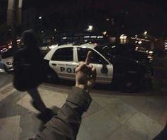 a police car parked in front of a building at night with someone holding up their hand