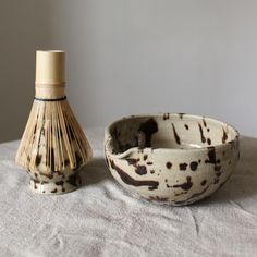 a white and brown bowl sitting next to a wooden bottle on top of a table