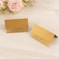 two cards with gold laser cut on them and flowers in the background next to each other