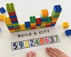 two hands are playing with legos and building blocks on the table next to a sign that says build a city