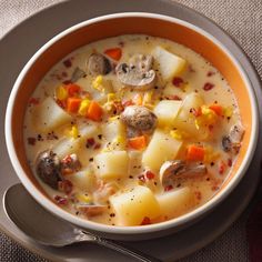 a bowl of soup with potatoes, carrots and meat on a gray plate next to a spoon